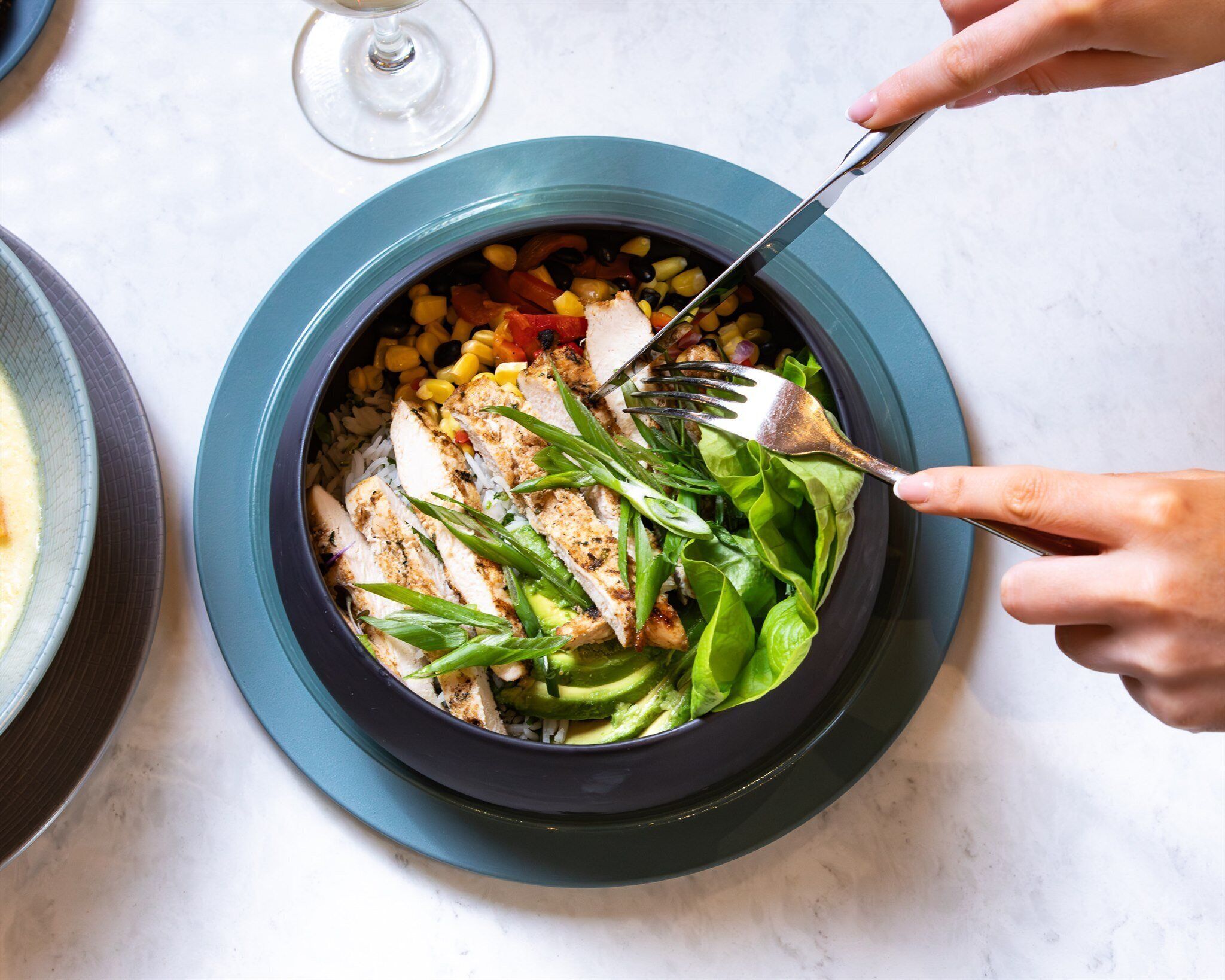 A bowl of salad with various vegetables and chicken, served on a dark plate.