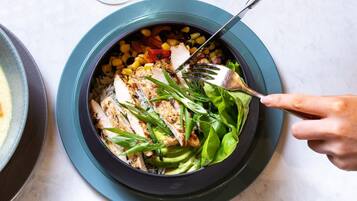 A bowl of salad with various vegetables and chicken, served on a dark plate.