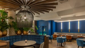Een modern restaurantinterieur met blauwe bekleden zitplaatsen, houten tafels en potplanten.