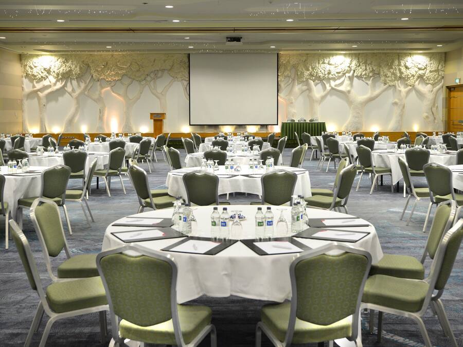 A conference room with round tables, green chairs, and a large screen at the front.
