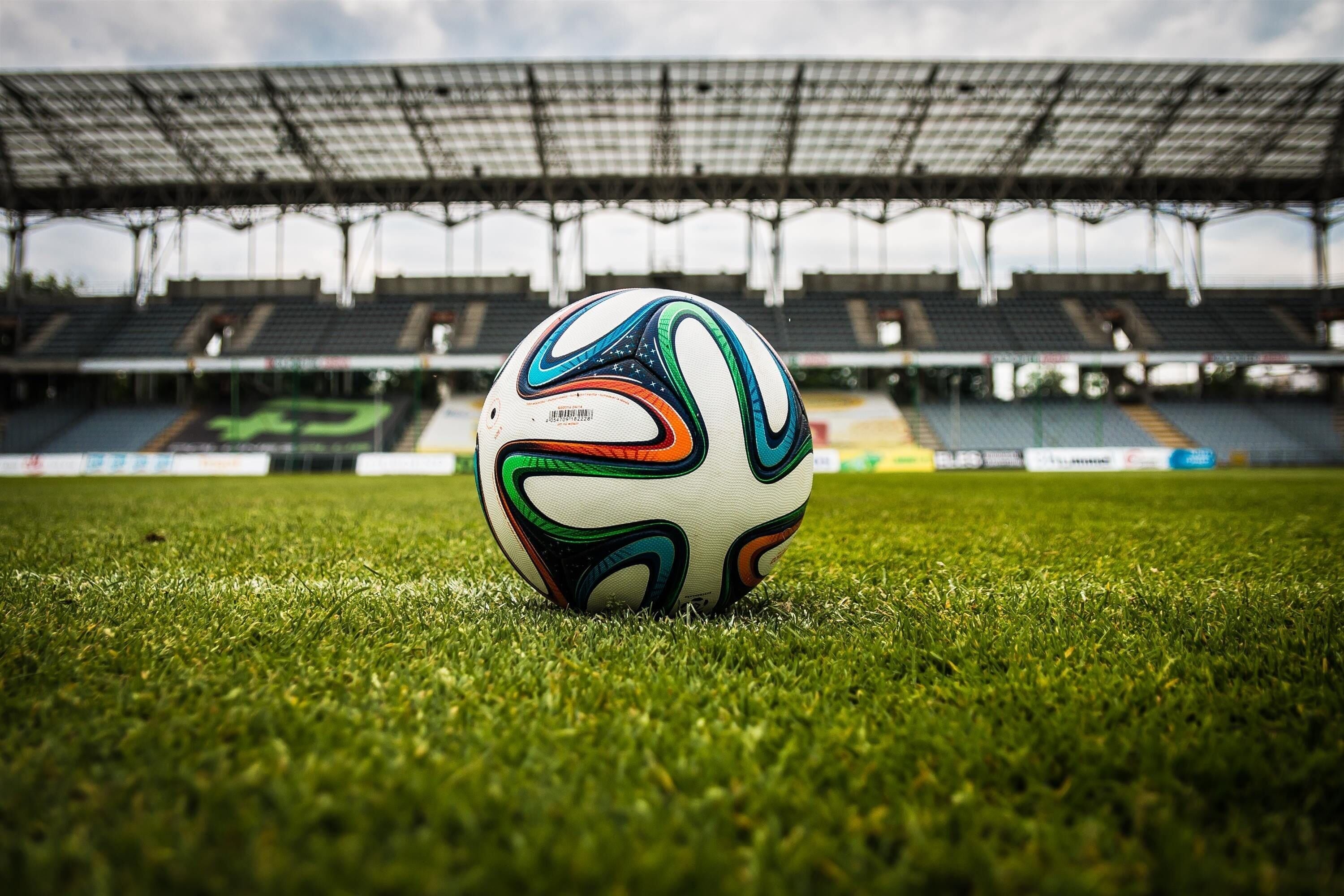 A soccer ball on a grassy field in an empty stadium.