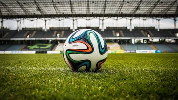 A soccer ball on a grassy field in an empty stadium.