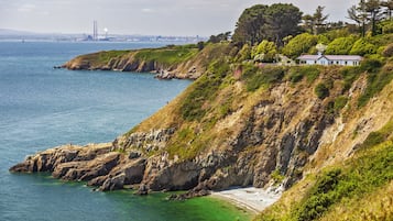 A coastal landscape with a cliff, beach, and a house on the hillside.
