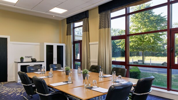 A conference room with a large table, chairs, and a view of the outdoors through large windows.