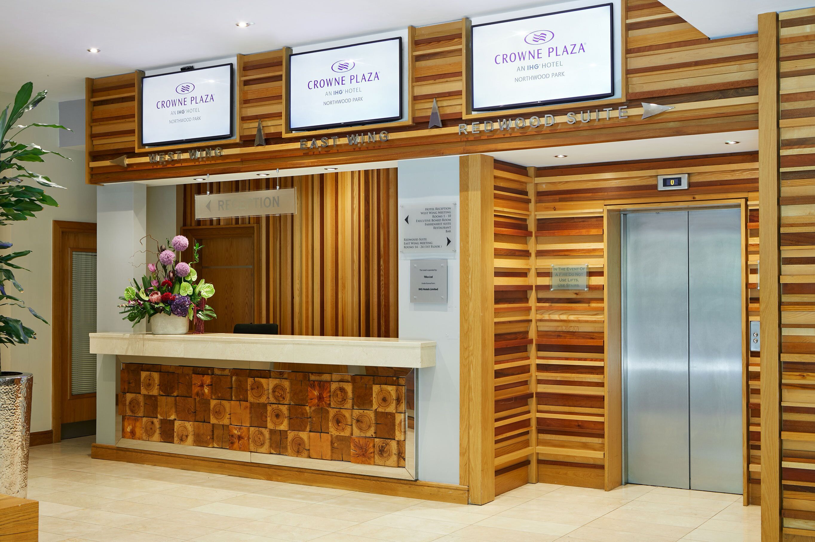 A hotel reception desk with a wooden panel design, a reception area, and an elevator.