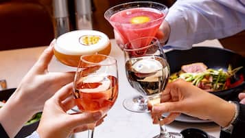 A group of people toasting with various drinks, including a cocktail with a fruit garnish, a glass with a creamy beverage, and a wine glass.
