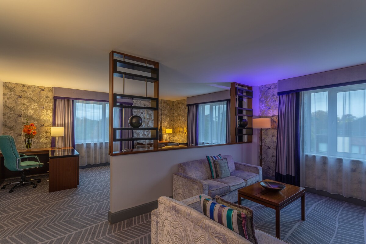 Une chambre d’hôtel équipée d’un canapé, d’un fauteuil, d’un bureau et d’un grand miroir.