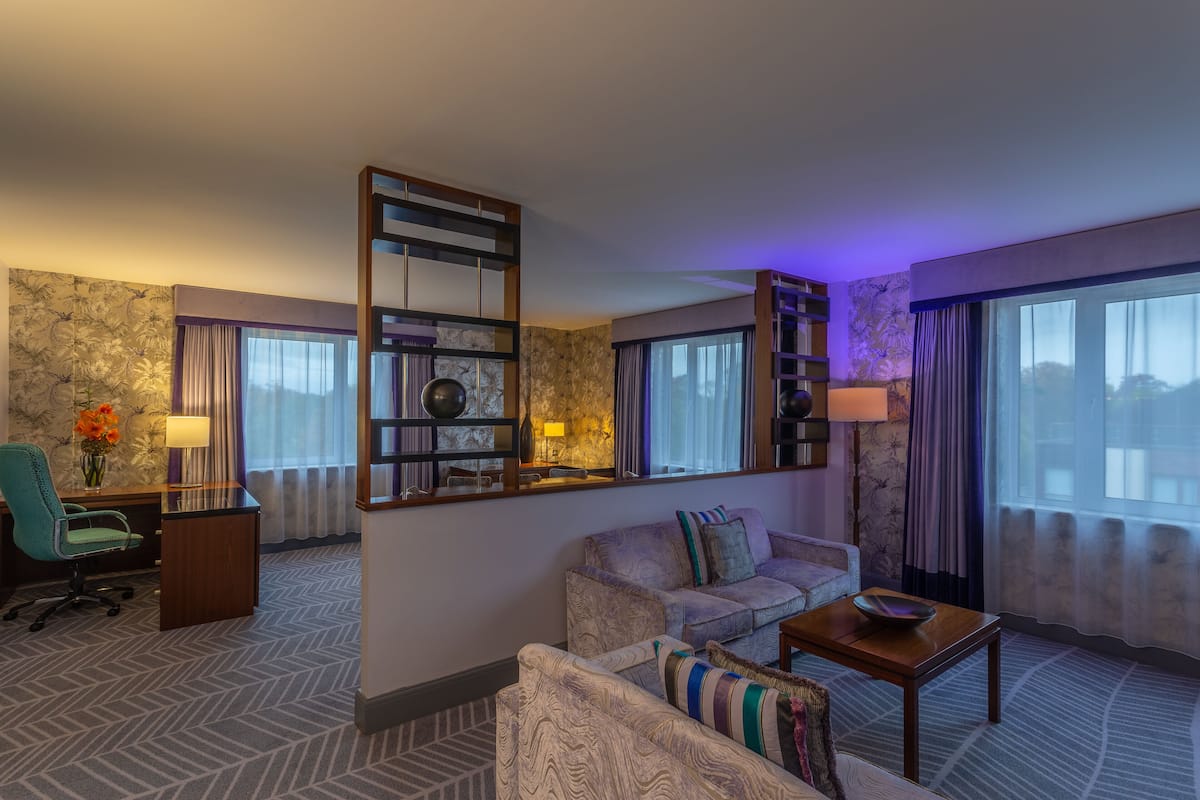 A hotel room with a sofa, armchair, desk, and a large mirror.