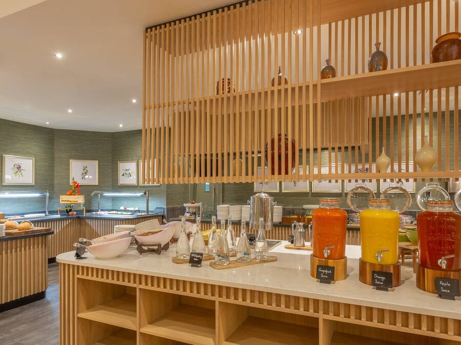 Un bar où l’on prend le petit-déjeuner, équipé de différents distributeurs de jus, une cloison en lattes de bois et un comptoir où sont exposés des produits alimentaires.