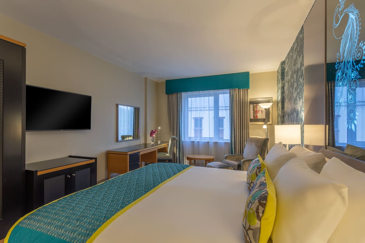 A hotel room with a large bed, a desk with a chair, a television, and a window with curtains.