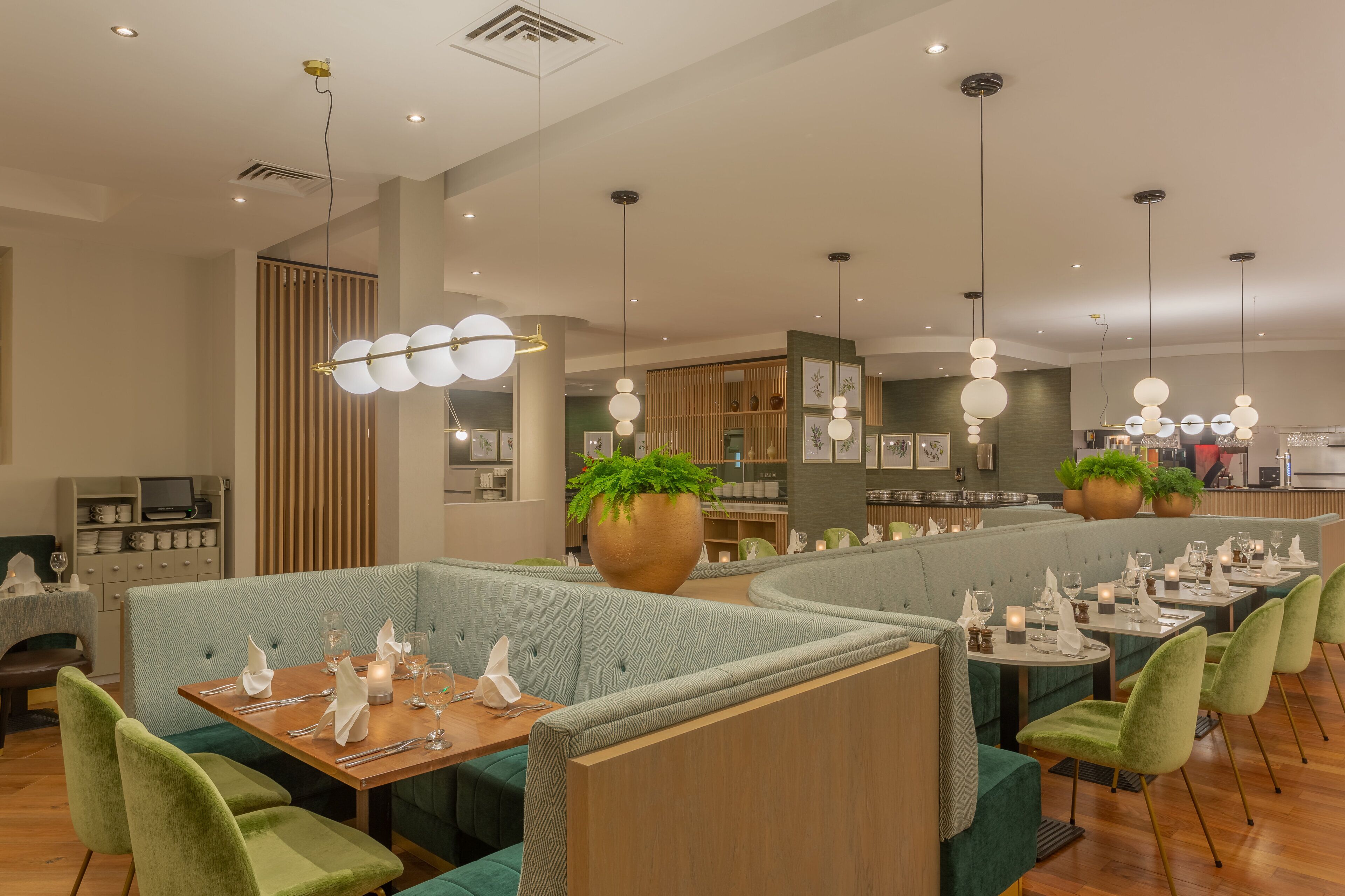 A restaurant with green upholstered booths, wooden tables, and pendant lighting.