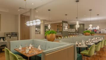 A restaurant with green upholstered booths, wooden tables, and pendant lighting.