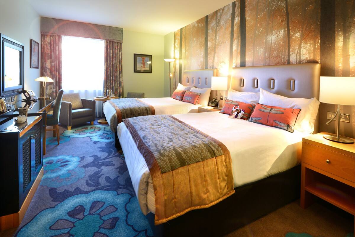 A hotel room with two beds, a desk, and a chair.