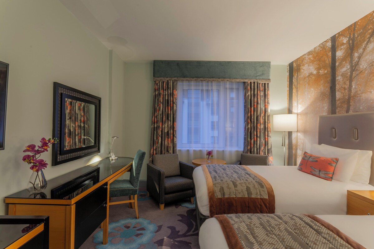 Une chambre d’hôtel avec un lit, un bureau, une chaise, une lampe et un tableau au mur.