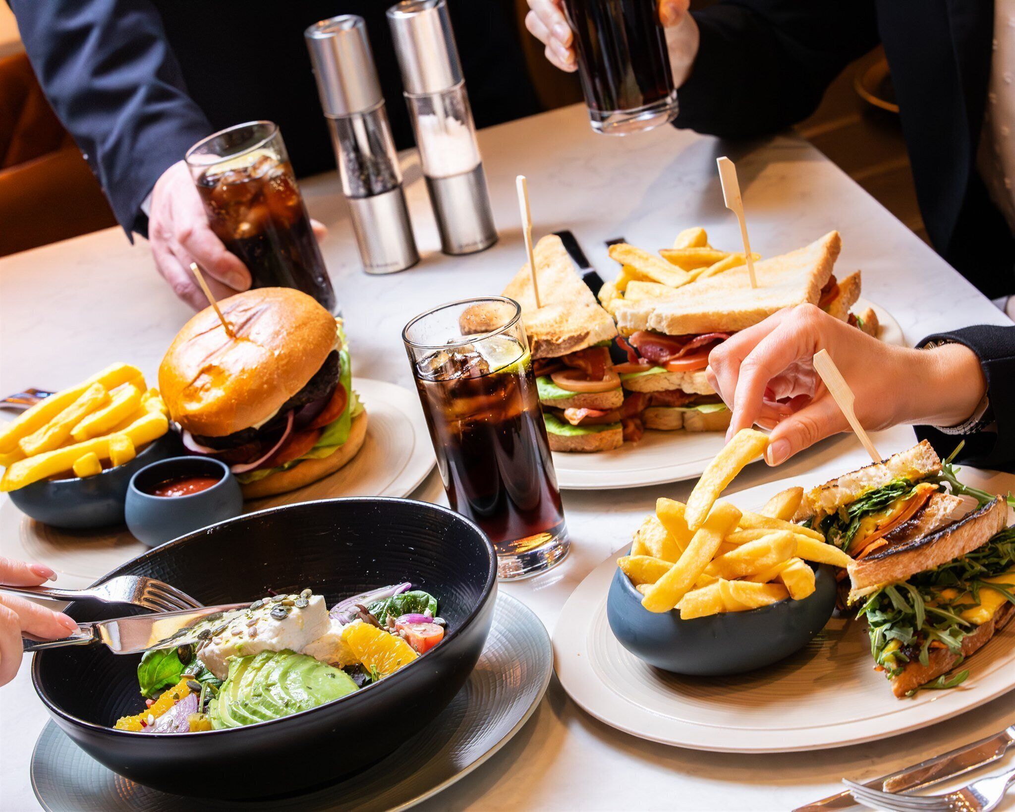 A dining table with various food items including burgers, sandwiches, fries, and a salad.