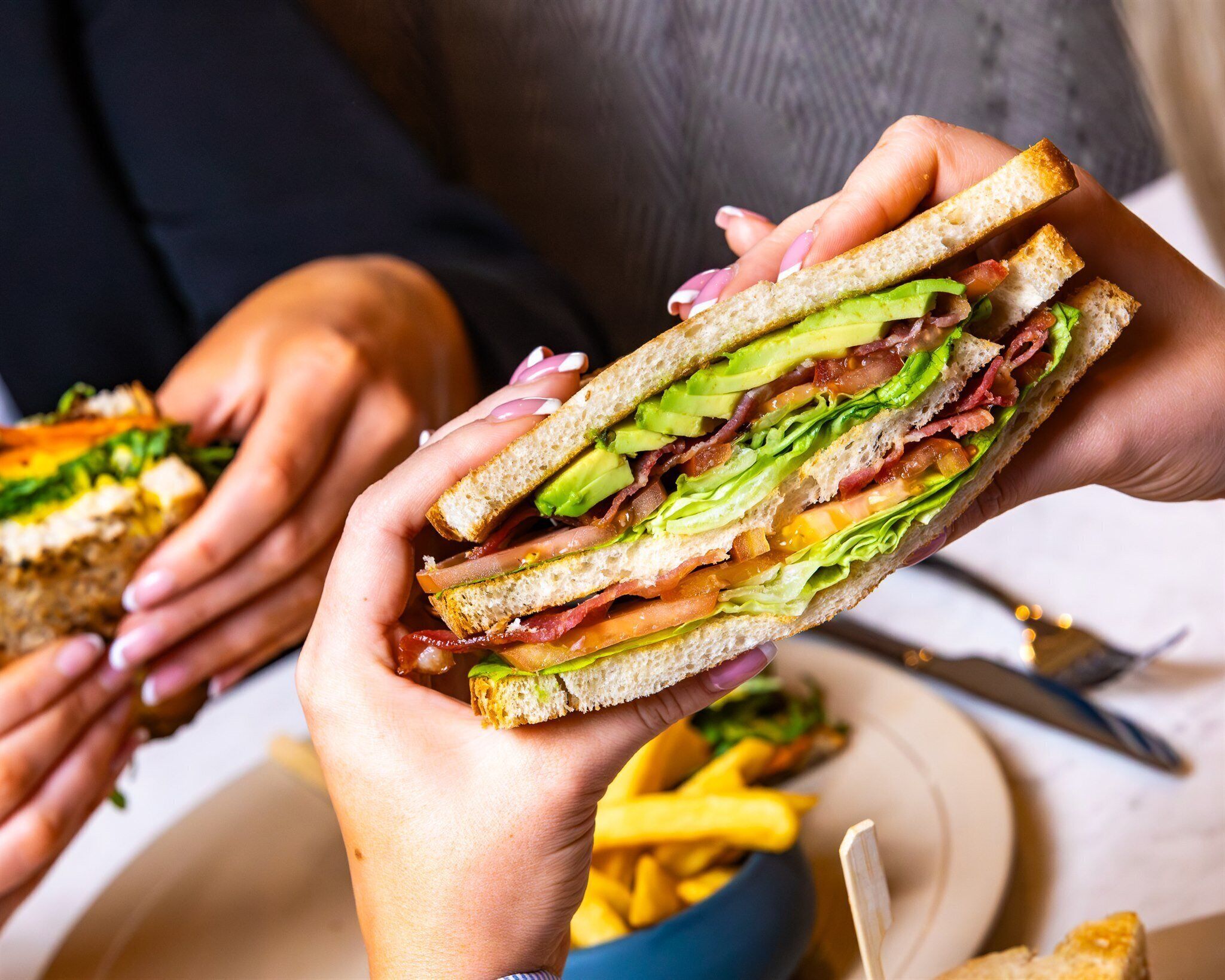 Una persona sosteniendo un sándwich con capas visibles de lechuga, tomate y otros ingredientes.