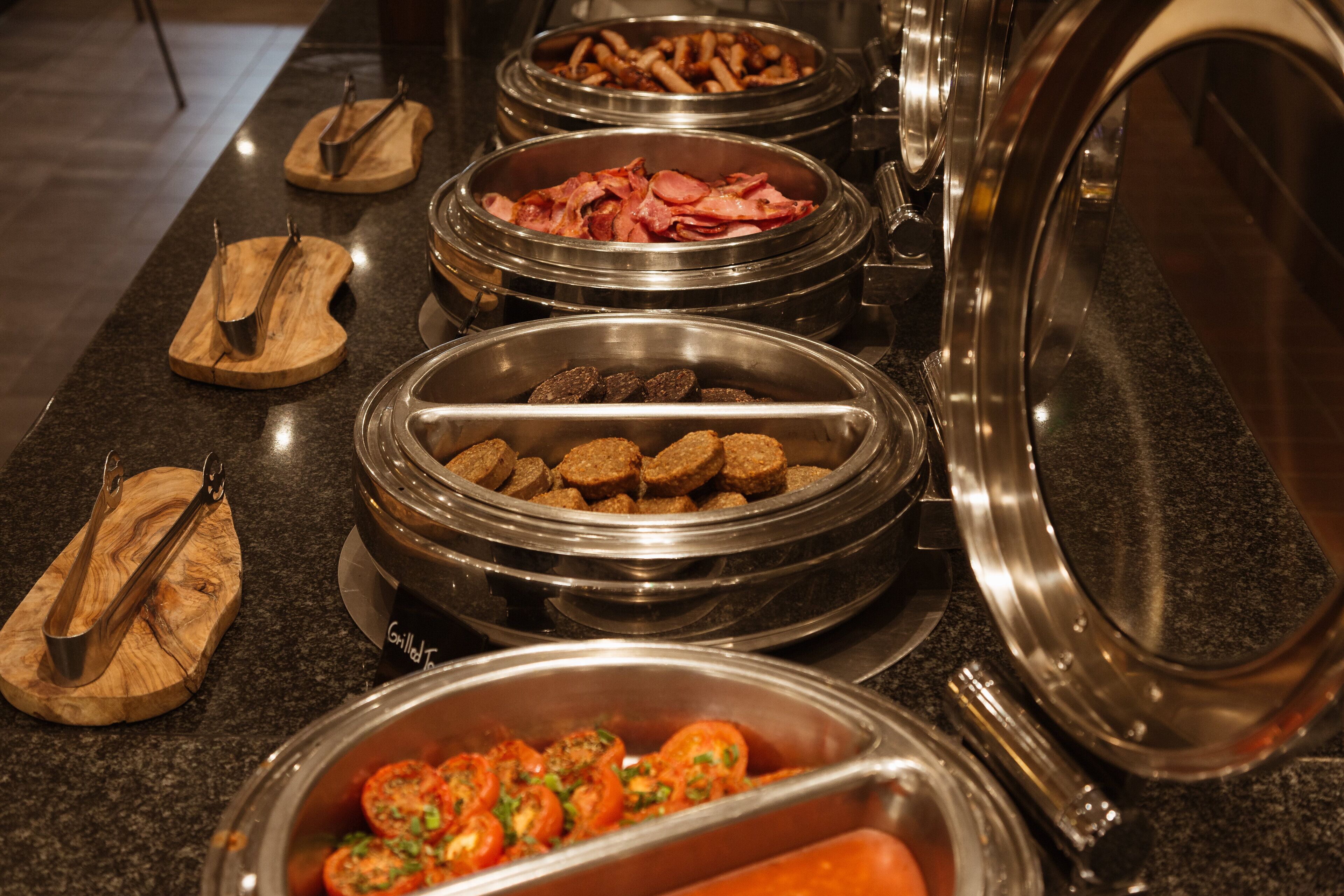 Buffet amb diferents aliments, com ara salsitxes, bacon i pollastre a la planxa.