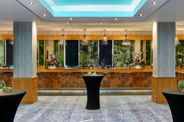 A bar area with a high ceiling, recessed lighting, and a view of greenery through large windows.