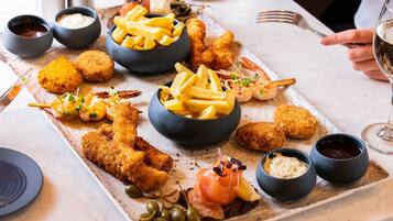 Una bandeja de mariscos con diversas frituras, incluyendo camarones y pescado, acompañada de papas fritas y salsas para mojar.
