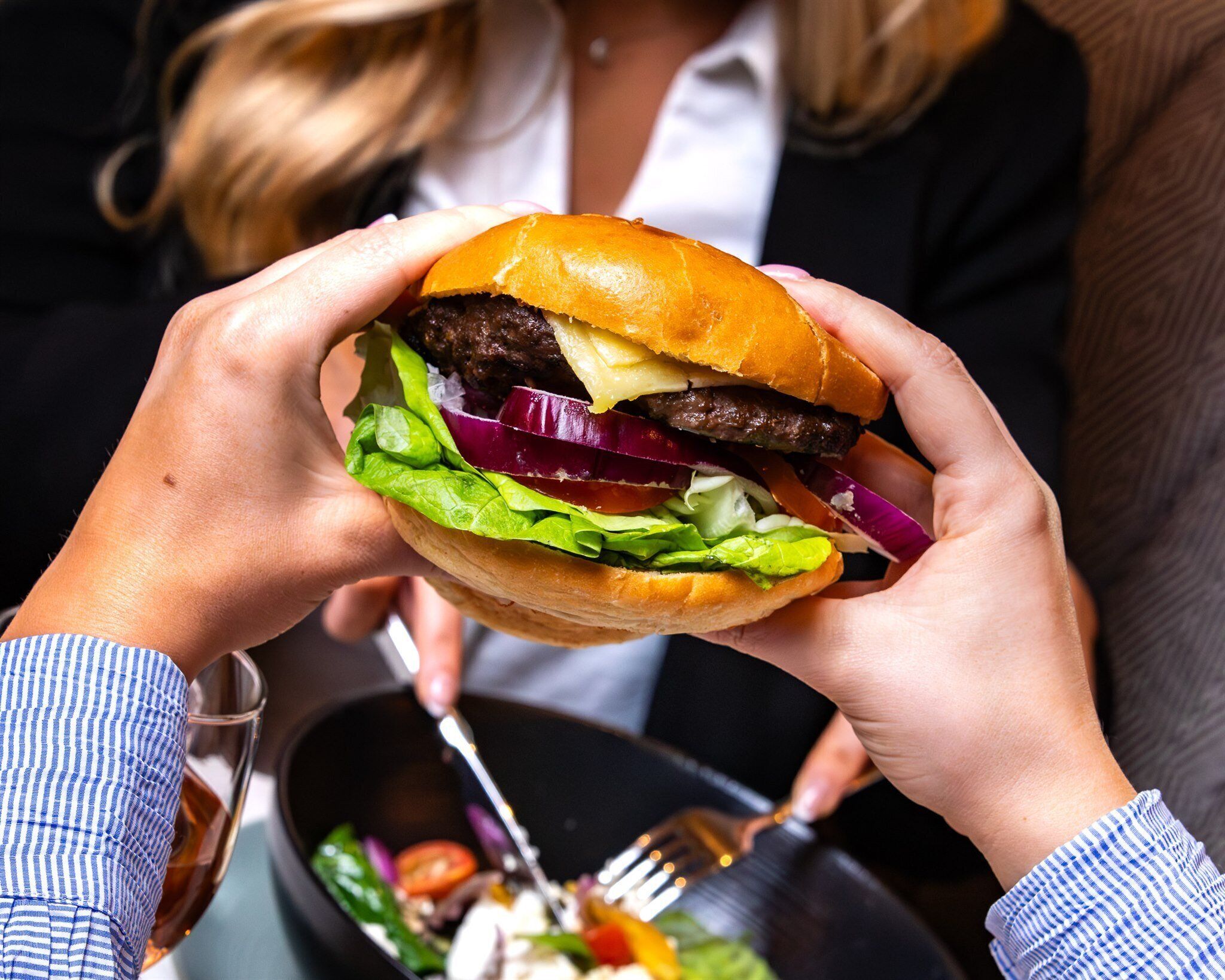 En person holder en burger, hvor ingredienser som salat, tomat og rød løg er tydelige.