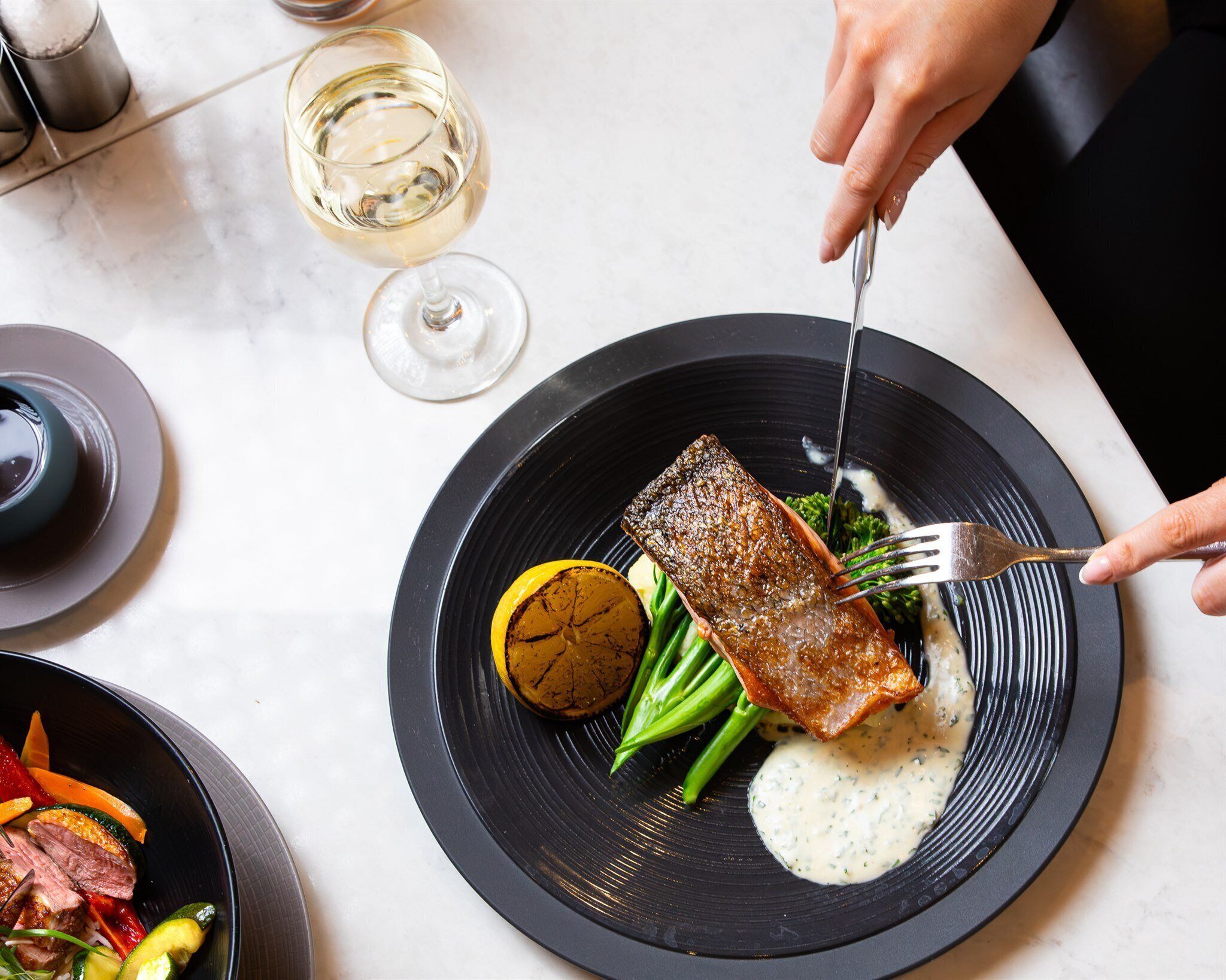 A plate with a piece of grilled fish, green beans, a grilled vegetable, and a creamy sauce.