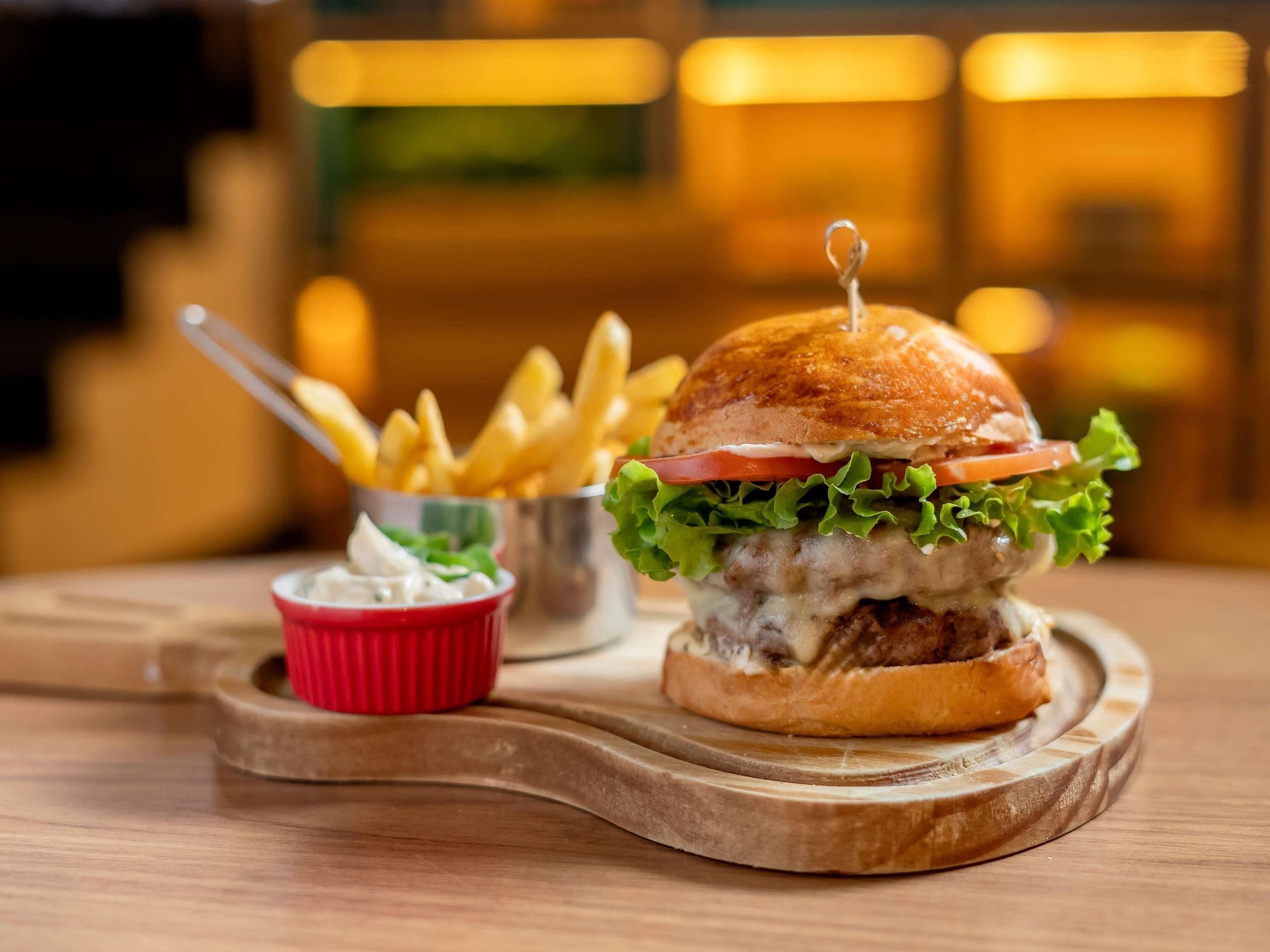 Una hamburguesa con lechuga, tomate y pan, acompañada de papas fritas y un pequeño recipiente con salsa sobre una tabla de madera.
