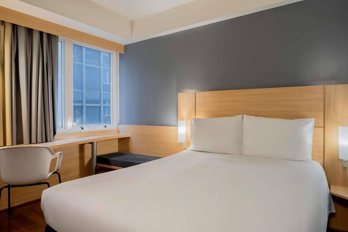 Une chambre d’hôtel avec un lit, un bureau, une chaise et une fenêtre avec des rideaux.