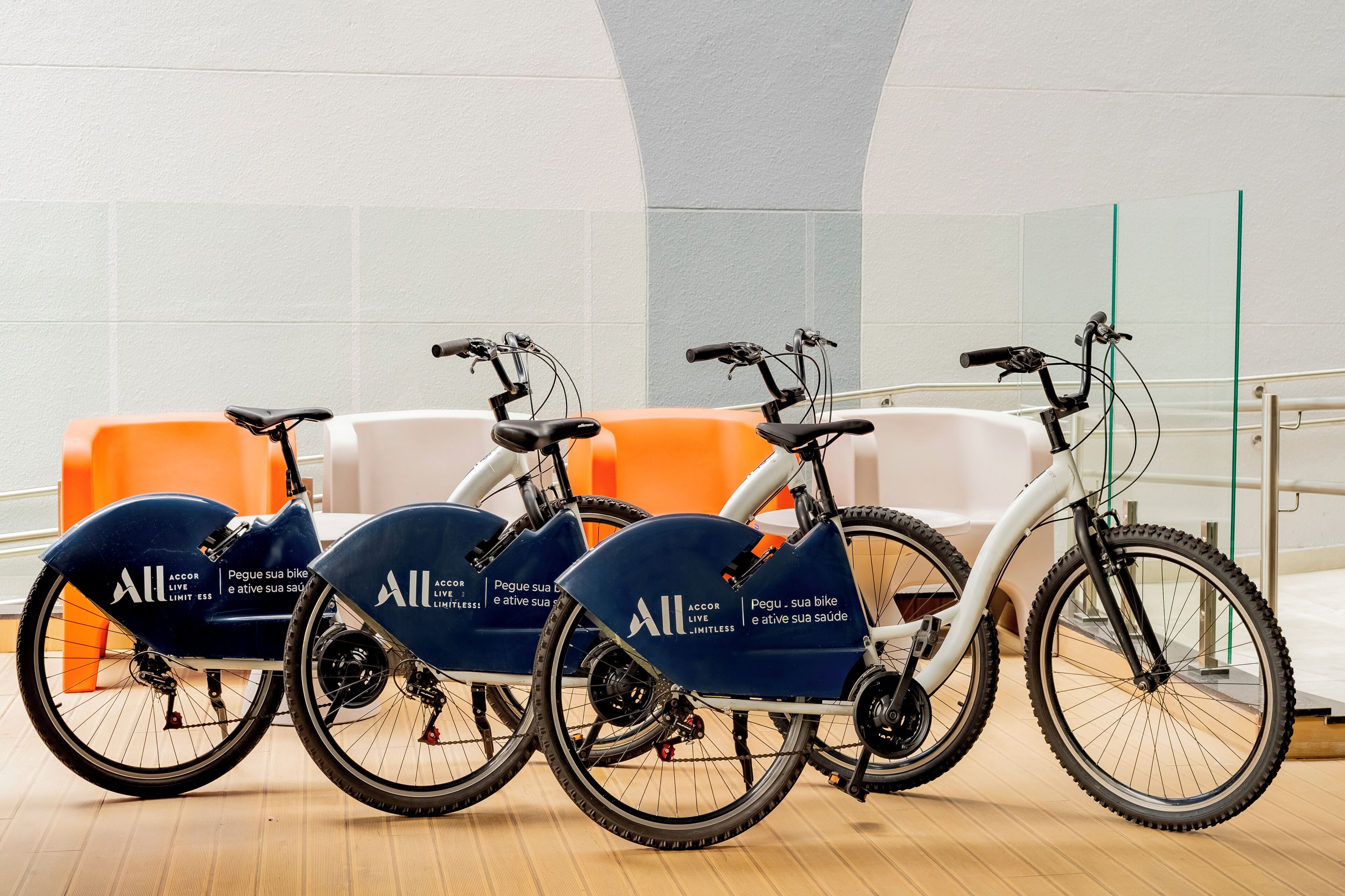 Three stationary bikes with 'All' branding in a room with a white ceiling and orange seating.