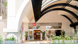 Una entrada de edificio moderno con una escalera que lleva a un restaurante llamado 'SPONTA PIZZA BAR' y un restaurante 'ibis' cercano.