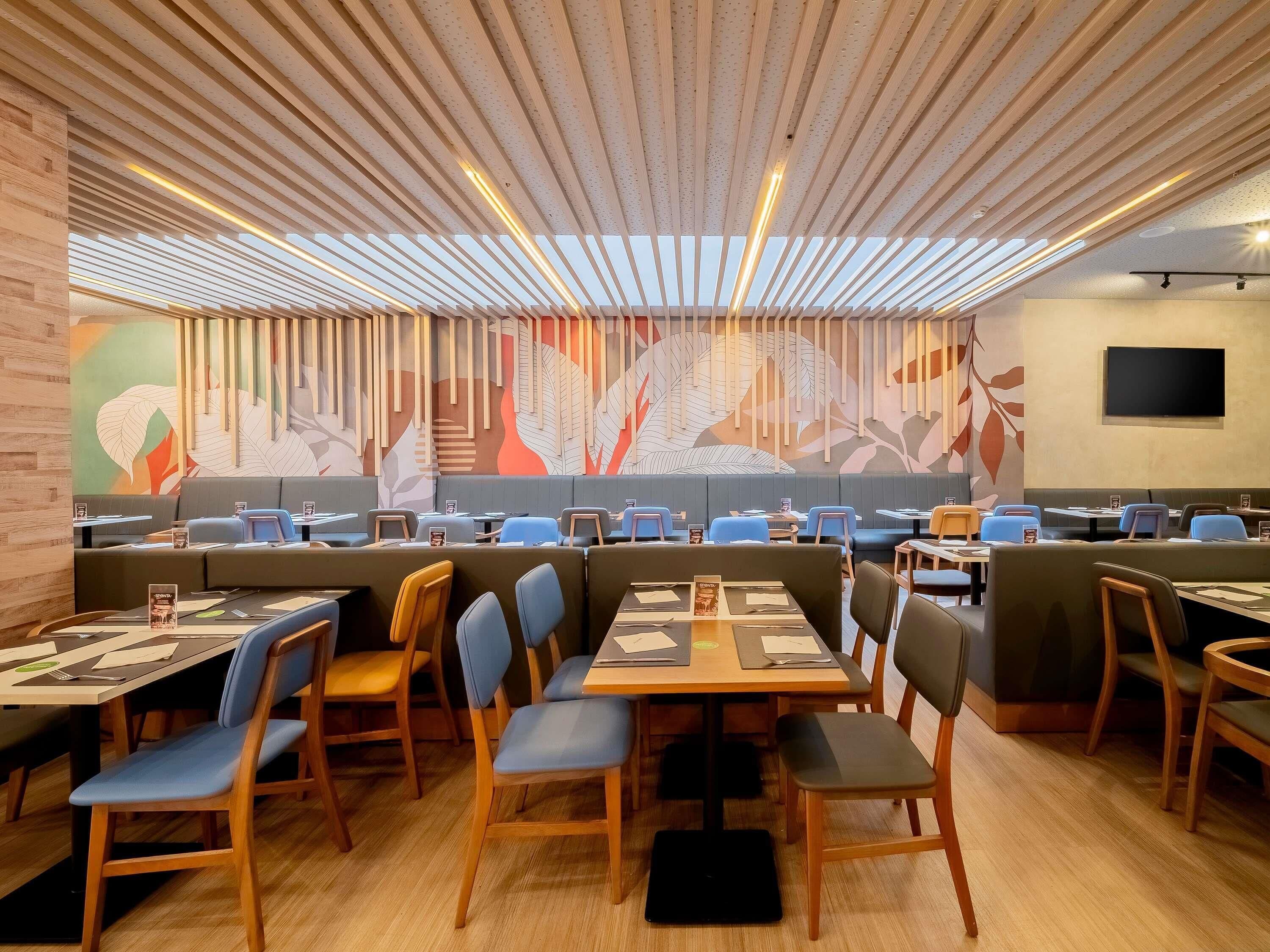 Um restaurante com cabines e mesas, piso de madeira e teto com padrão de folhas.