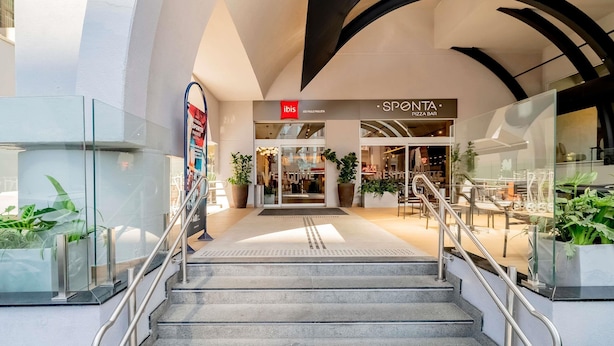 Un interior moderno con una escalera que lleva a un restaurante llamado 'SPONTA PIZZA BAR'.