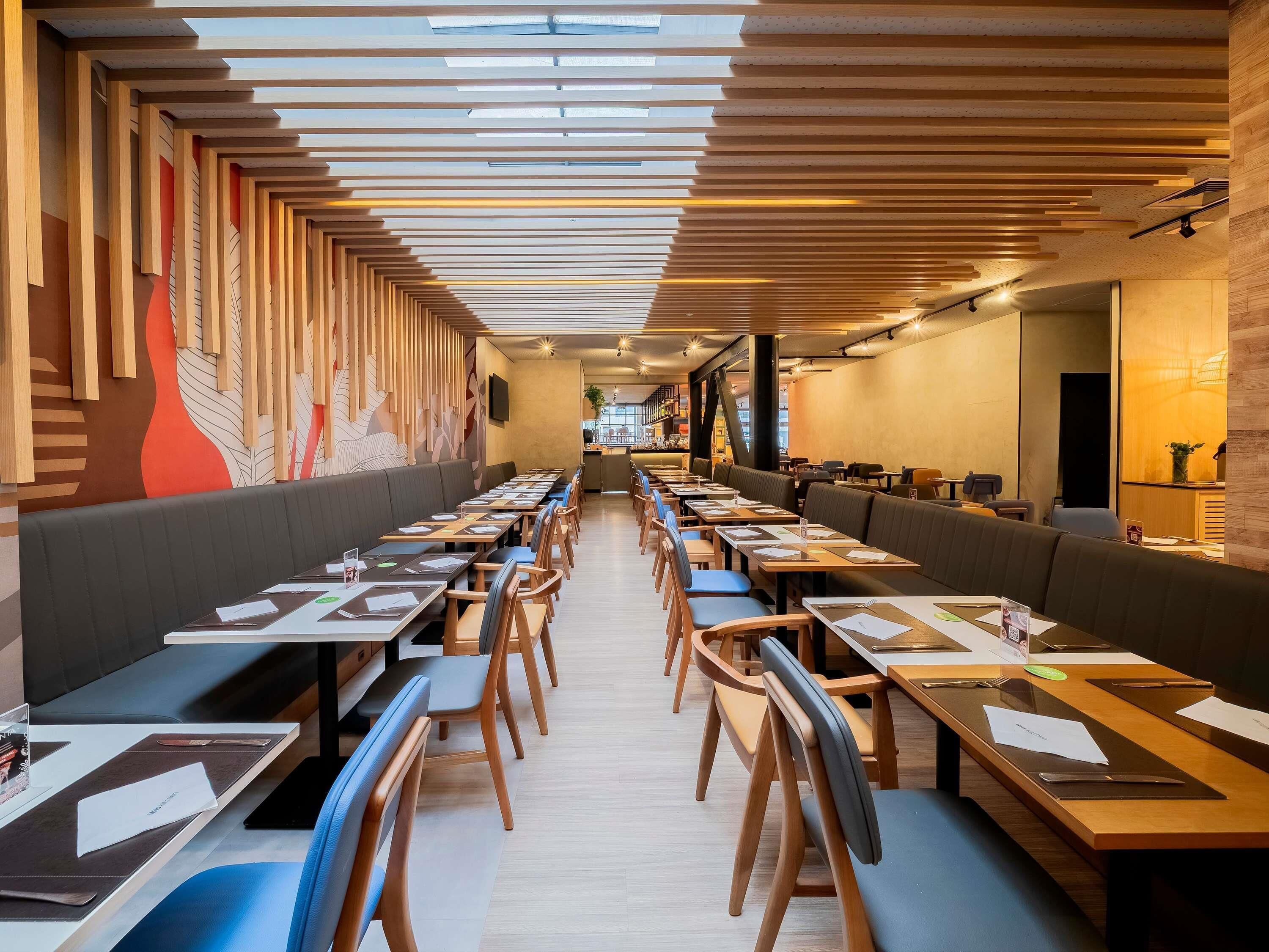 A modern restaurant with long tables, booths, and a high ceiling with wooden slats.