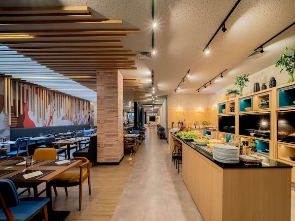 A modern restaurant interior with wooden paneling, a long counter with food displays, and a seating area with tables and chairs.