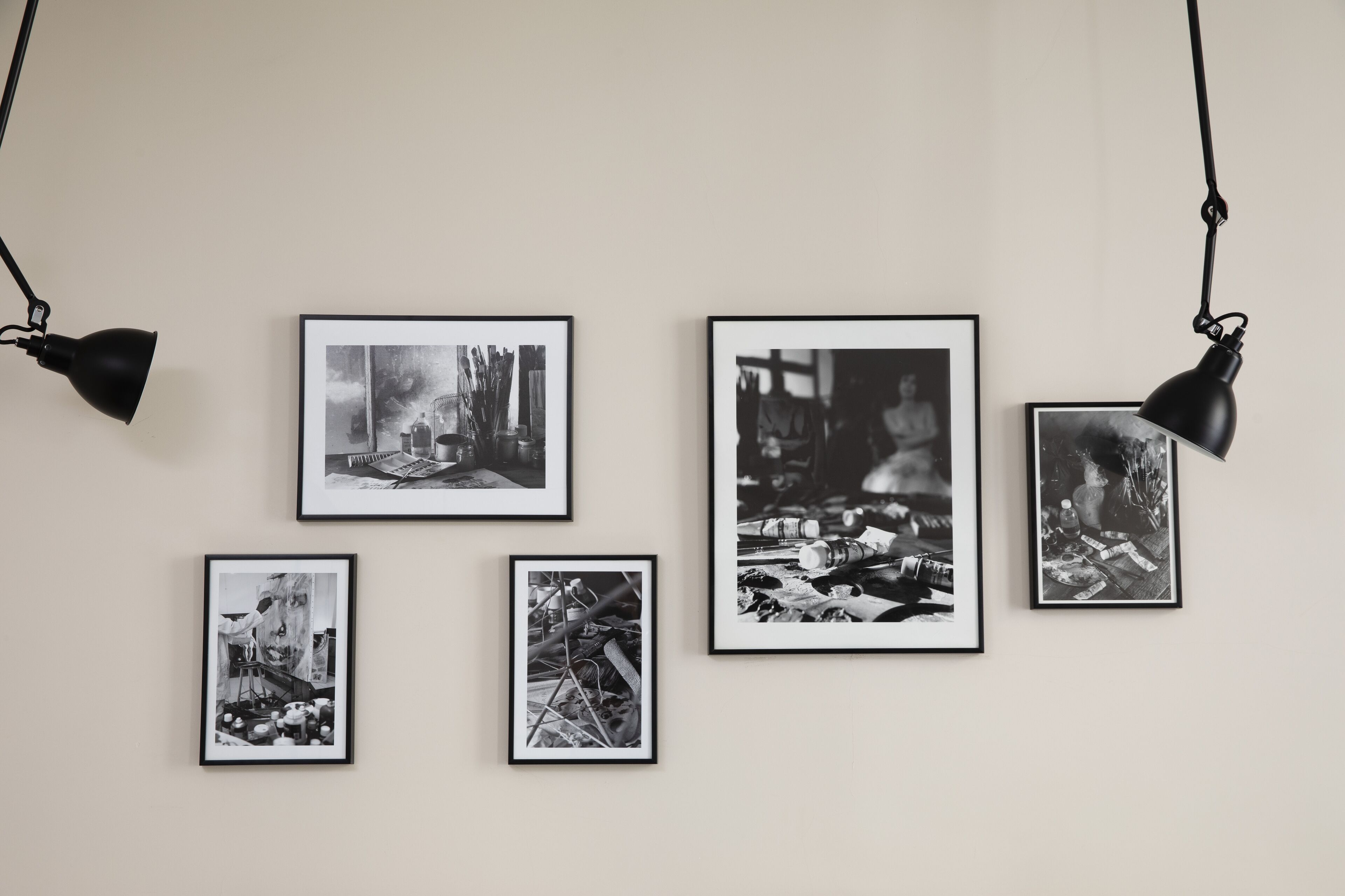 A wall with five black and white photographs and two hanging black spotlights.