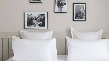 Una cama bien hecha con sábanas y almohadones blancos, fotografías en blanco y negro en la pared y un cabecero de madera.