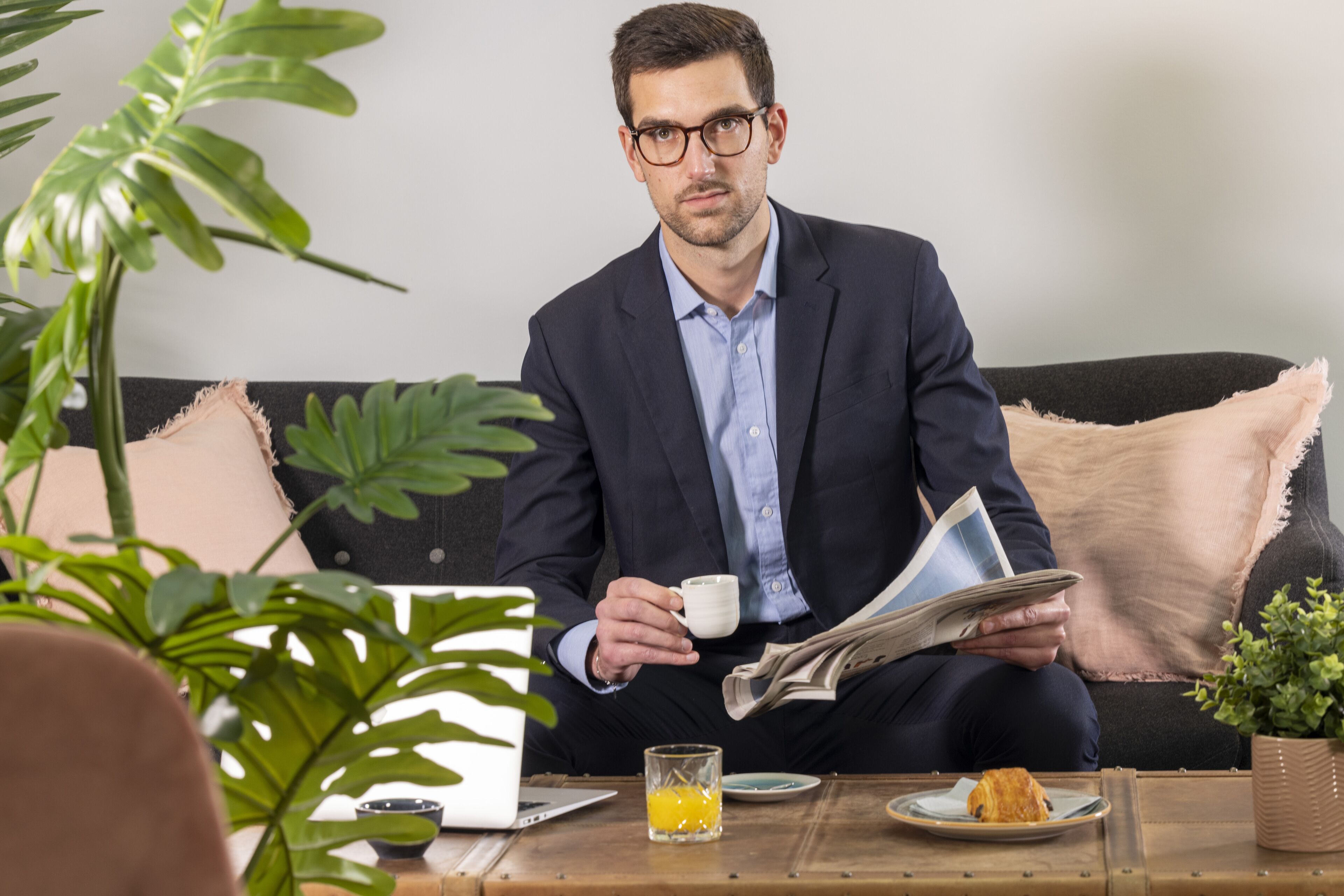 A person sitting on a couch with a laptop, a newspaper, a cup, and a glass of orange juice on a table.