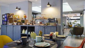 Una cocina moderna con cafetera, estantes con frascos y una zona de comedor con una mesa para dos.
