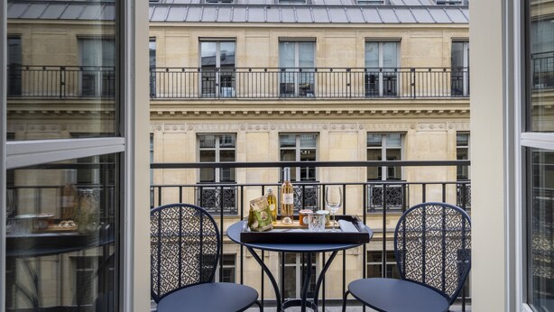 A balcony with a table set for two, featuring a bottle of wine, a glass, and a small bag. - Hôtel Hélios Opéra (Paris)