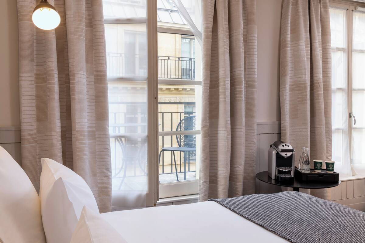 A hotel room with a bed, a small table with a coffee maker, and a view of the outside balcony.