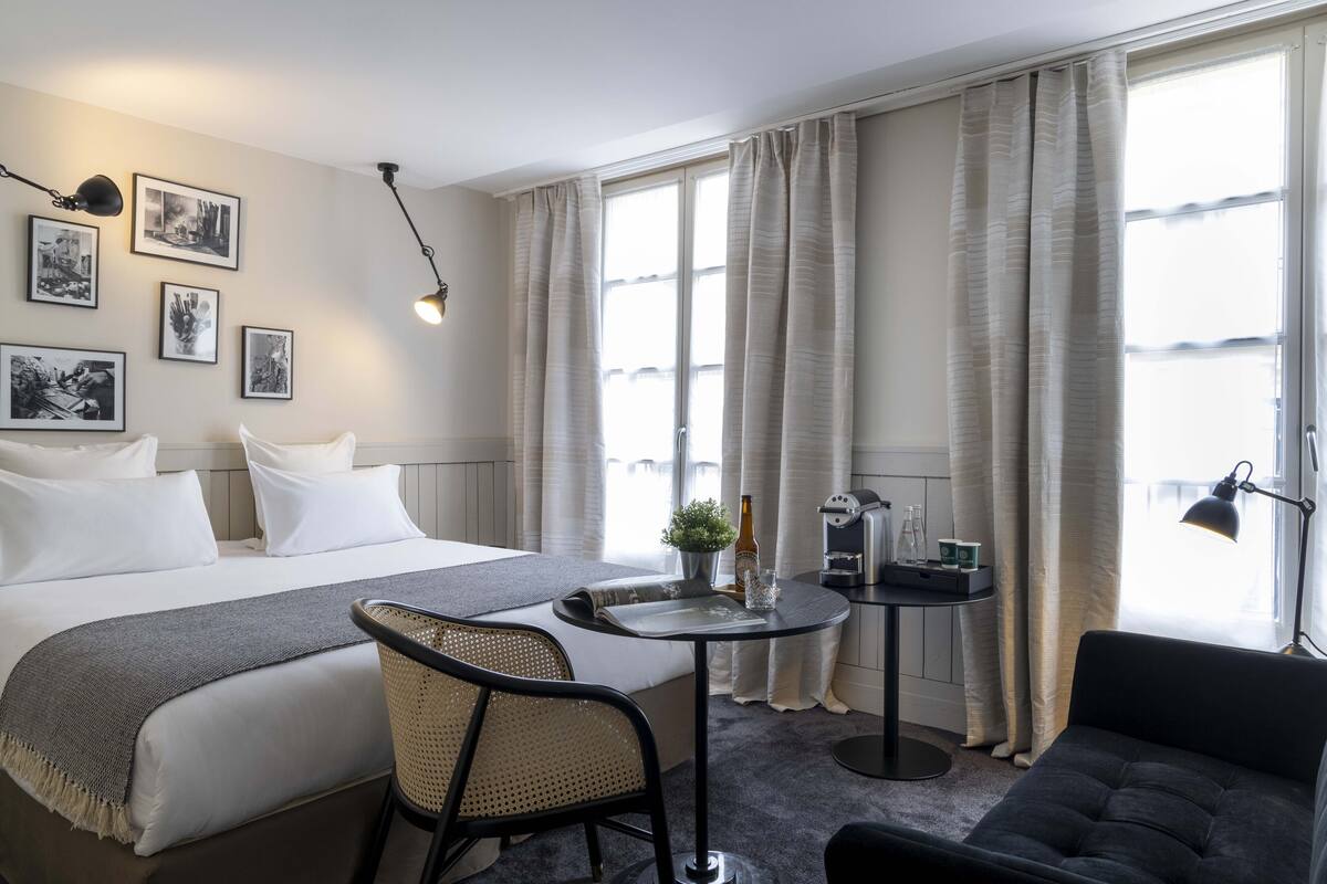 A hotel room with a bed, a small table with a plant, a coffee machine, and a sofa.