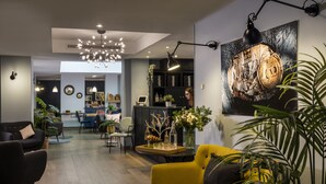 A modern living room with a yellow sofa, a black armchair, and a dining area in the background. - Hôtel Hélios Opéra (Paris)