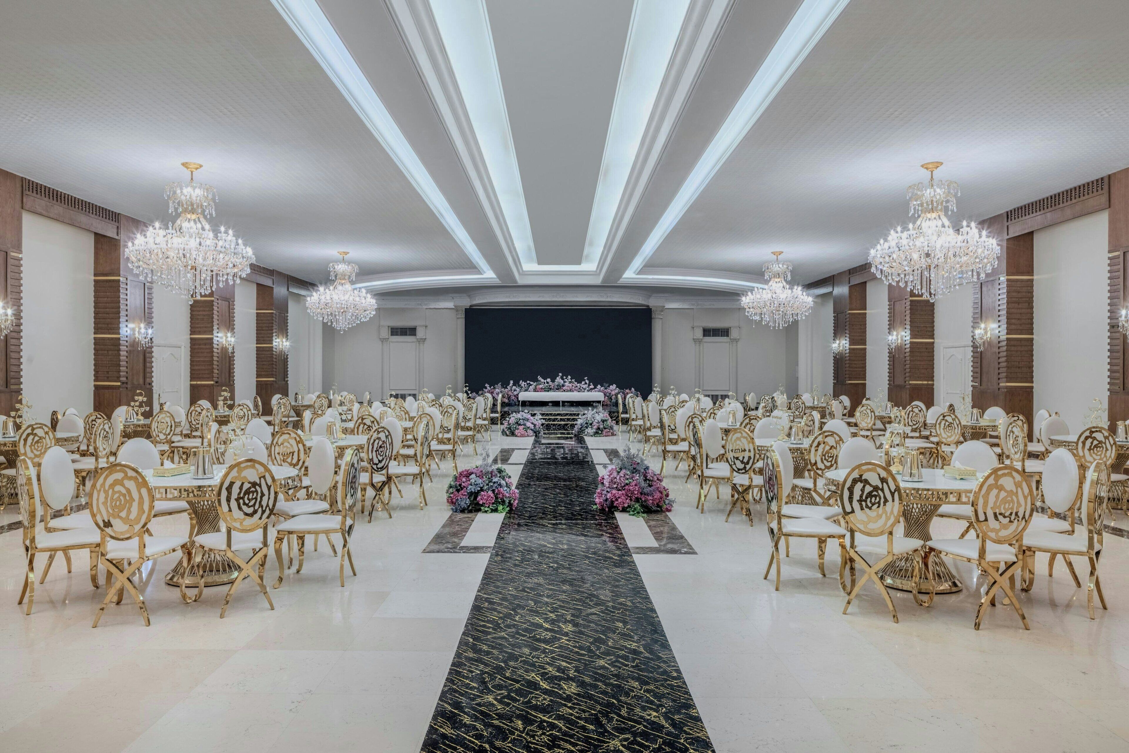 Un salón de banquetes con filas de mesas redondas, sillas doradas y candelabros.