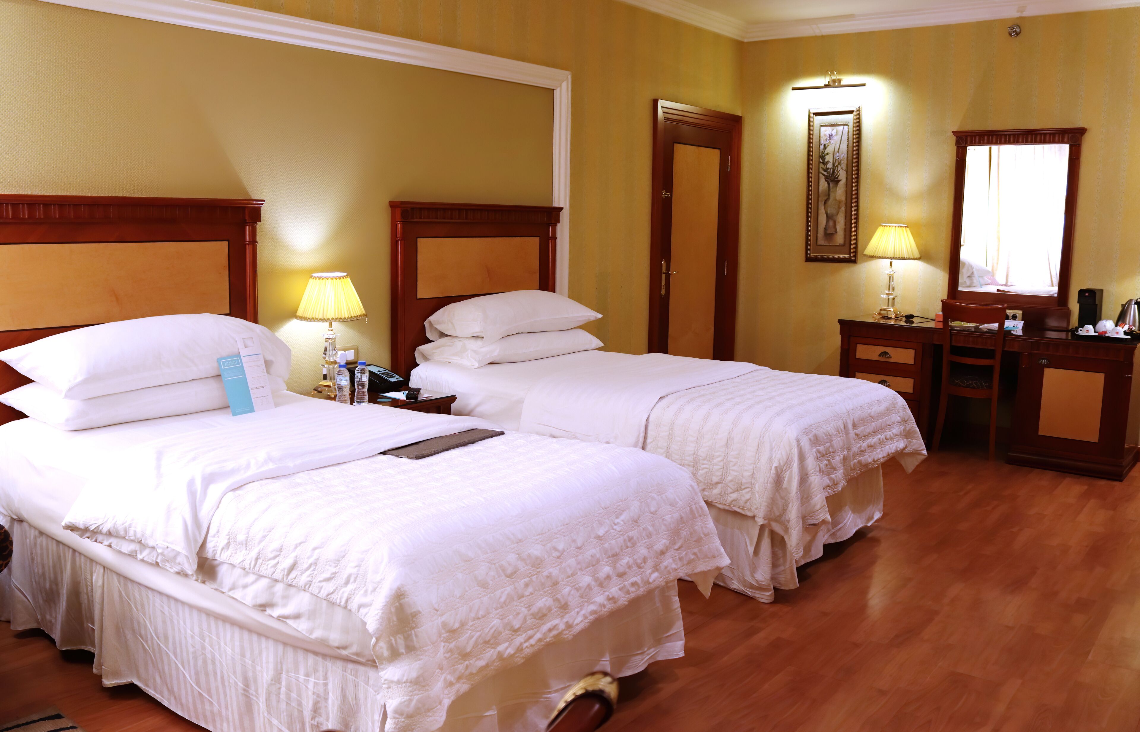 A hotel room with two beds, a desk with a chair, a lamp, and a mirror.