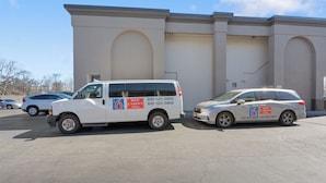 En hvid varevogn og en hvid minivan parkeret foran en bygning med et stort hvælvet vindue og en dør.