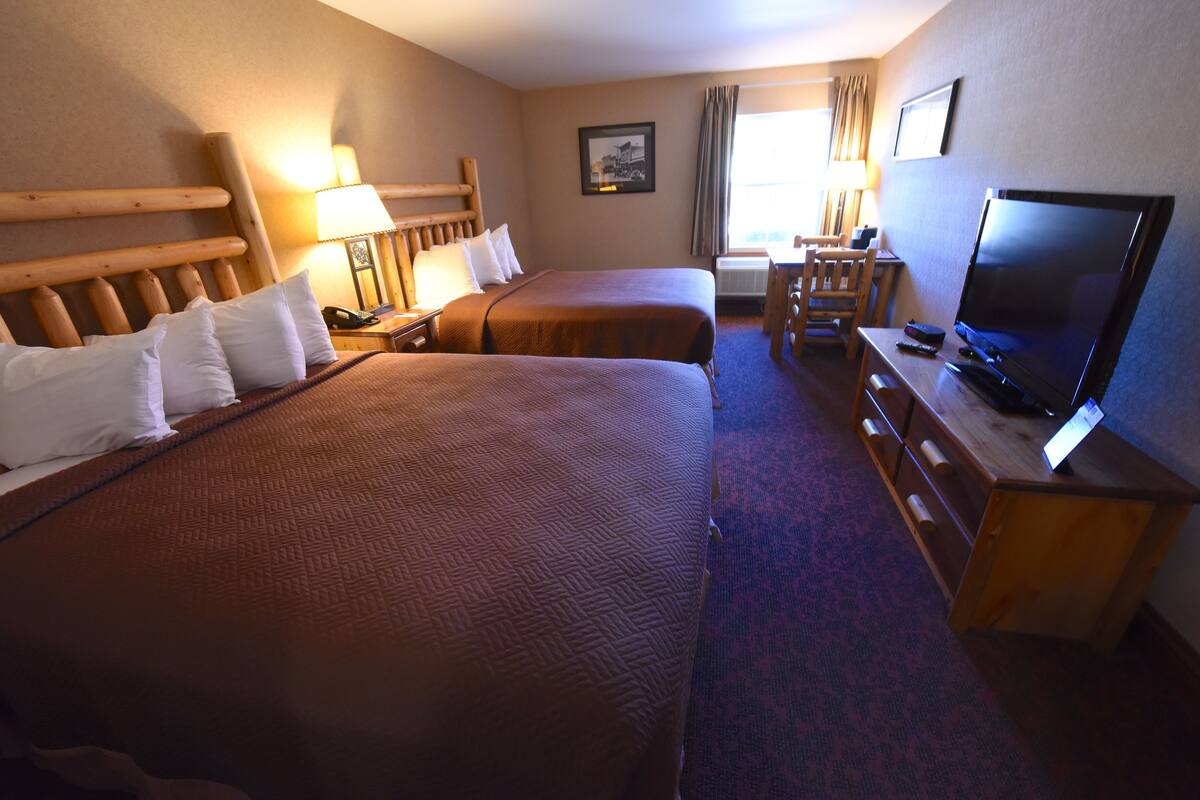 A hotel room with two beds, a desk with a television, and a chair.