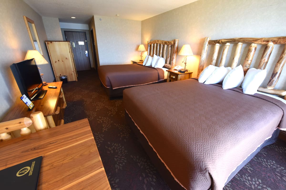 A hotel room with two beds, a desk with a computer, a TV, and a wooden headboard.