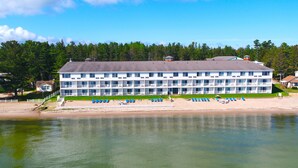 A multi-story hotel with a flat roof, located near a beach with blue chairs and umbrellas. - Bridge Vista Beach - Hotel & Convention Center (Mackinaw City)