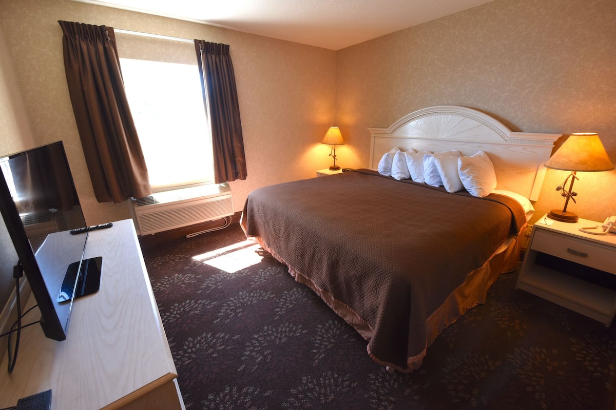 A hotel room with a bed, two bedside lamps, a TV, and a desk.
