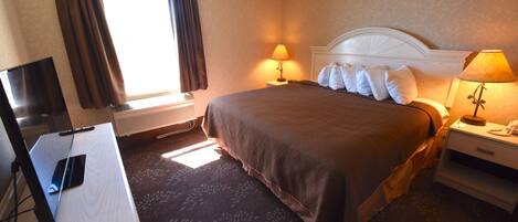 A hotel room with a bed, two bedside lamps, a TV, and a desk.