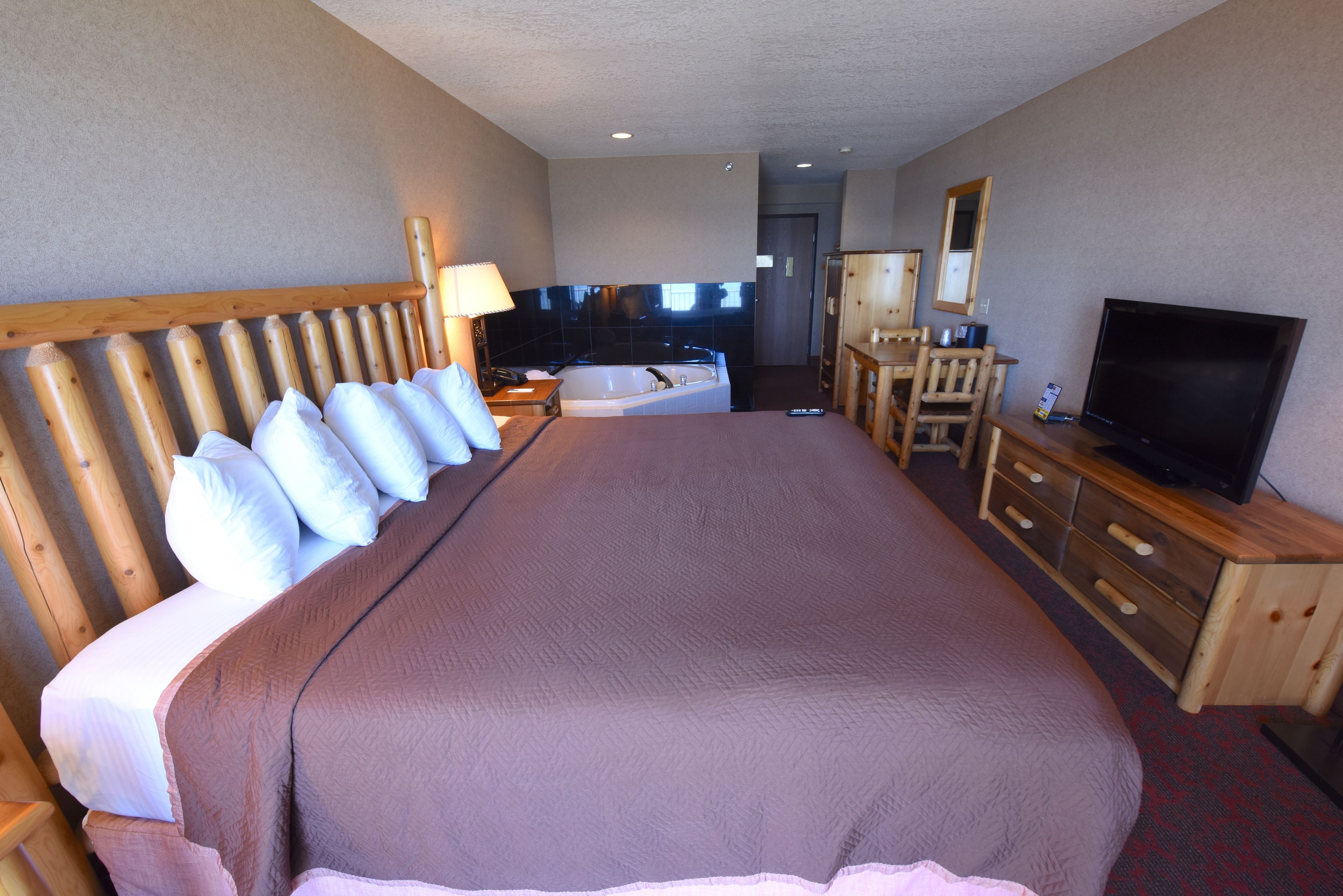 Habitación de hotel con una cama grande, cabecero de madera, televisor, escritorio y baño con bañera.